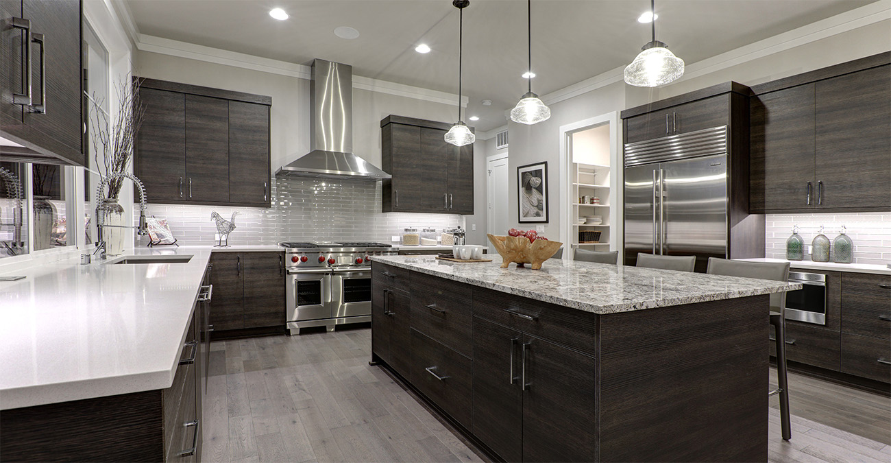 Modern kitchen with dark wood cabinets, large island with granite countertop, stainless steel appliances, pendant lights, white subway tile backsplash, and light wood flooring.